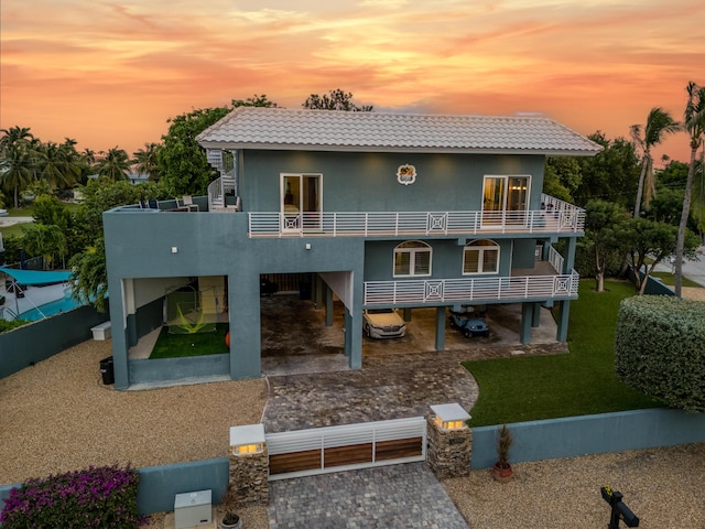 back of property with driveway, a balcony, a tiled roof, fence, and stucco siding