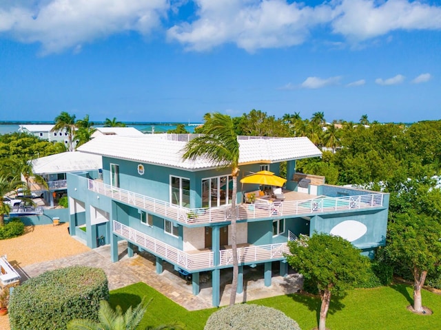 back of property with a tile roof, gravel driveway, a water view, and stucco siding