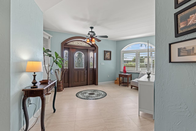 entryway with a textured wall, a ceiling fan, and baseboards