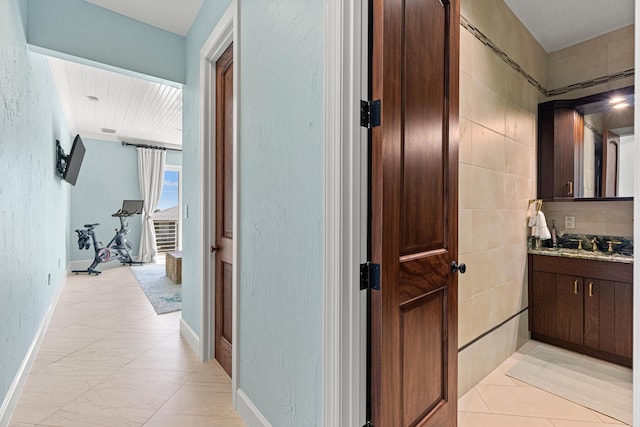 hall with a textured wall, tile walls, baseboards, and light tile patterned floors