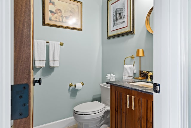 half bathroom featuring toilet, baseboards, and vanity