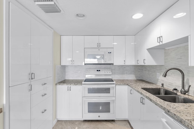 kitchen with white appliances, a sink, visible vents, white cabinets, and light stone countertops