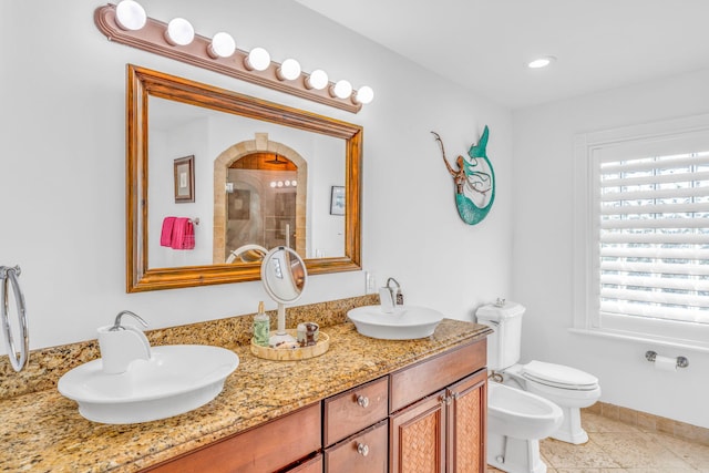 full bath featuring a tile shower, double vanity, a sink, and toilet