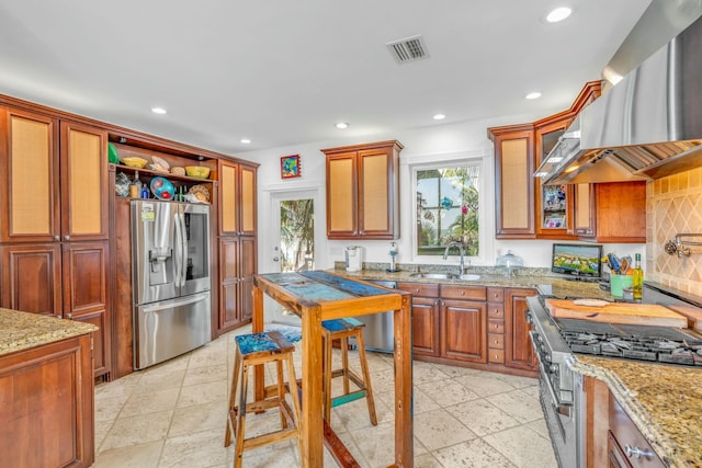 kitchen with stainless steel appliances, recessed lighting, a sink, light stone countertops, and wall chimney exhaust hood