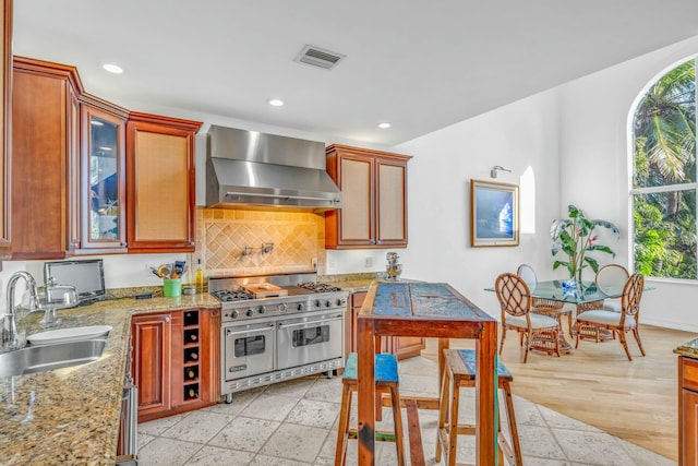 kitchen with visible vents, range with two ovens, wall chimney range hood, a sink, and recessed lighting