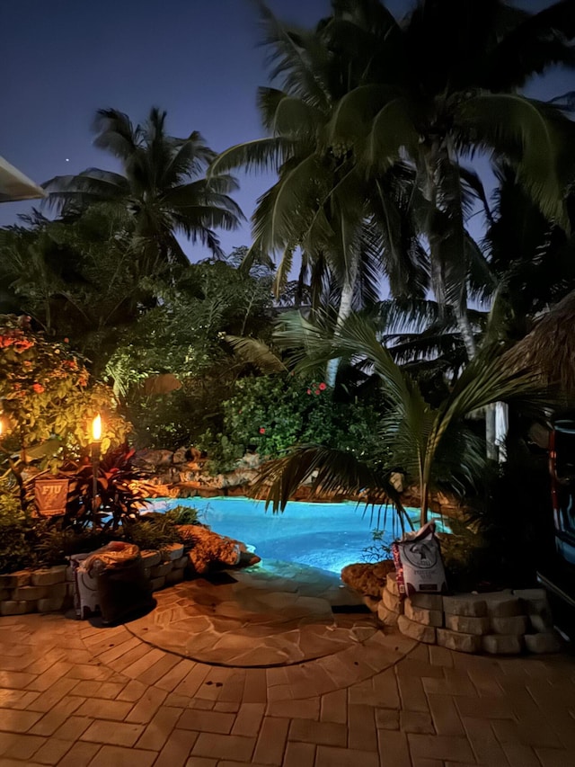 pool at night with an outdoor pool and a patio