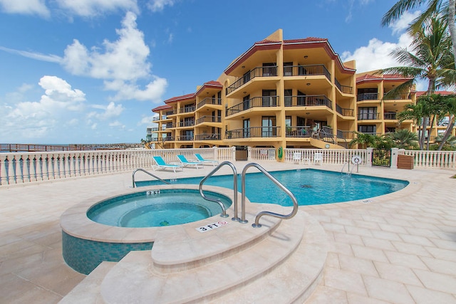 community pool with a patio, fence, and a hot tub