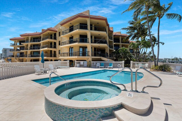 pool with a patio area, fence, and a hot tub
