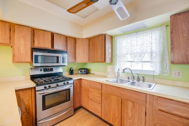 kitchen featuring light countertops, appliances with stainless steel finishes, a sink, and brown cabinets