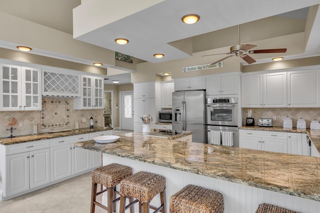 210 14th St, Key Colony, FL 33051 - kitchen featuring a breakfast bar, appliances with stainless steel finishes, glass insert cabinets, white cabinetry, and light stone countertops