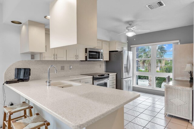 kitchen featuring visible vents, a peninsula, a sink, stainless steel appliances, and backsplash