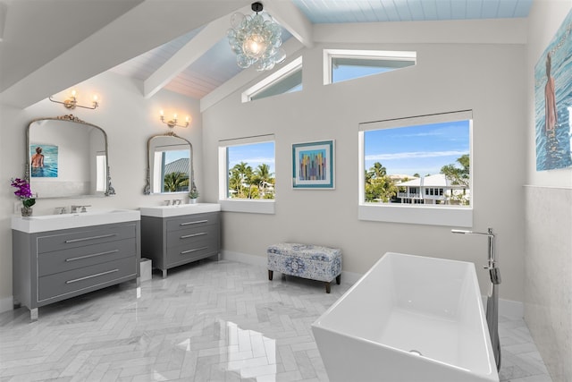 full bath featuring a notable chandelier, two vanities, a freestanding bath, beamed ceiling, and baseboards