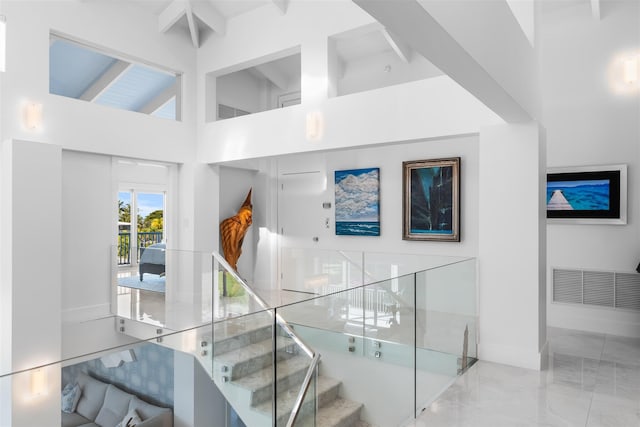 stairway with visible vents, baseboards, marble finish floor, a high ceiling, and beam ceiling