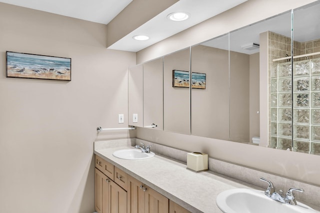 bathroom featuring double vanity, tiled shower, a sink, and recessed lighting