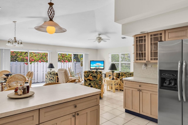 kitchen featuring pendant lighting, stainless steel refrigerator with ice dispenser, light tile patterned floors, light countertops, and glass insert cabinets