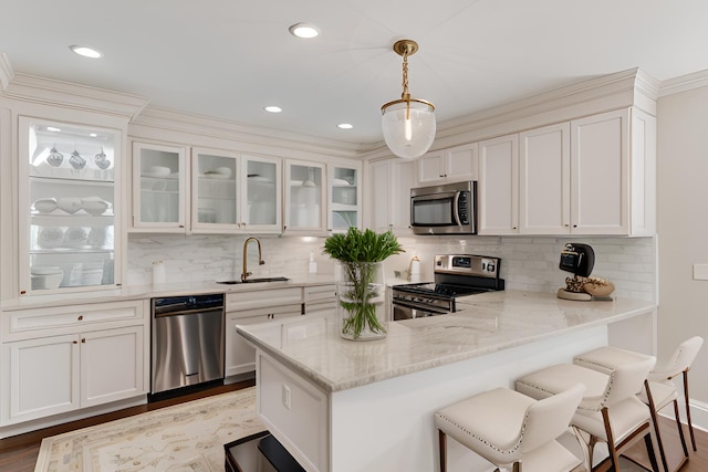 kitchen featuring decorative light fixtures, stainless steel appliances, glass insert cabinets, white cabinetry, and a sink