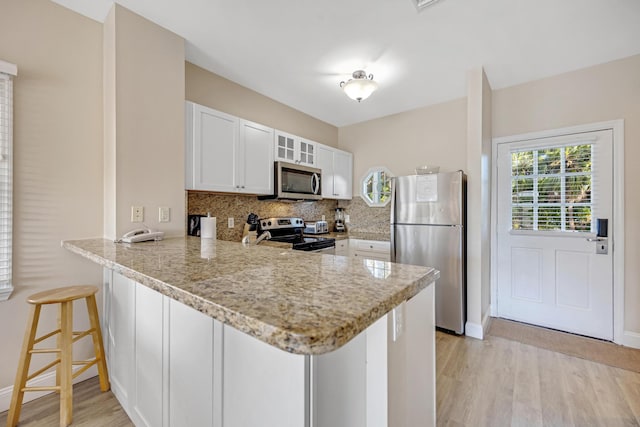 kitchen featuring stainless steel appliances, a breakfast bar, a peninsula, white cabinetry, and backsplash