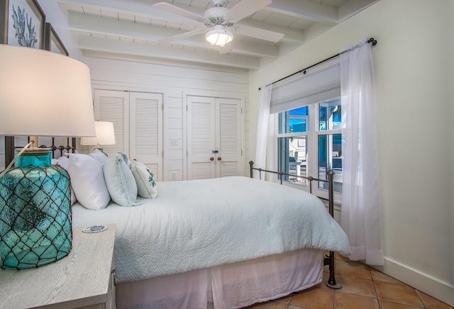 bedroom with two closets, ceiling fan, tile patterned flooring, beamed ceiling, and baseboards