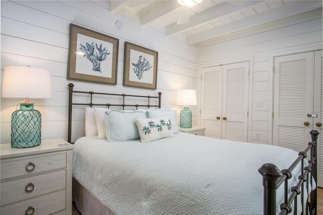 bedroom featuring wood walls, beam ceiling, and multiple closets