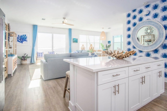 kitchen with ceiling fan, white cabinets, light wood-style floors, light countertops, and a kitchen bar