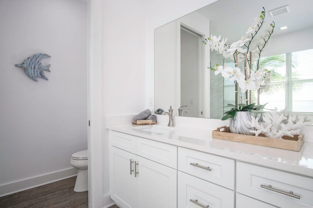 bathroom featuring toilet, wood finished floors, visible vents, vanity, and baseboards