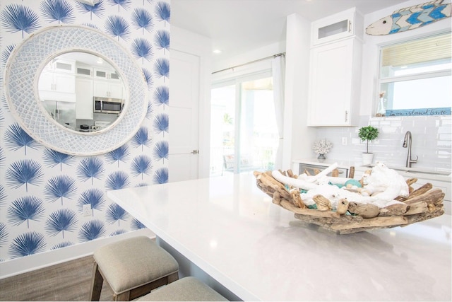 kitchen with light countertops, stainless steel microwave, decorative backsplash, glass insert cabinets, and white cabinetry