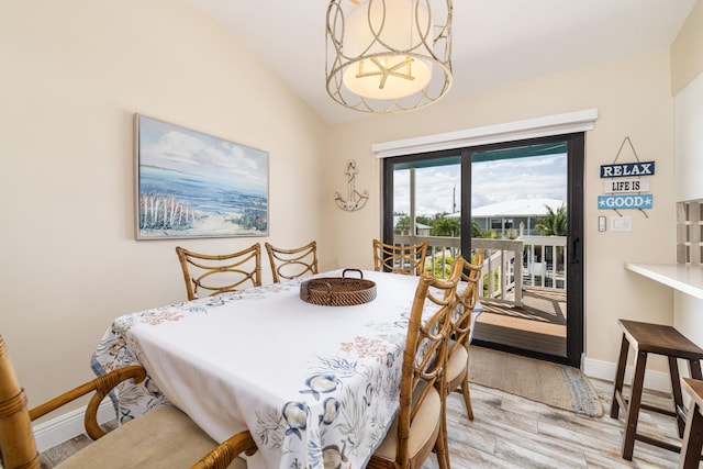 dining space featuring a notable chandelier, light wood-style floors, baseboards, and vaulted ceiling