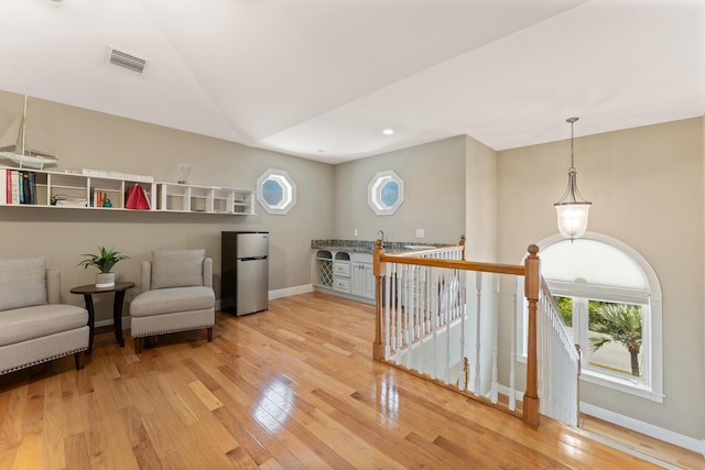 sitting room with an upstairs landing, light wood-style flooring, visible vents, and a healthy amount of sunlight