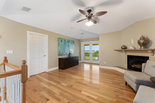 living room with ceiling fan, light wood-type flooring, a glass covered fireplace, visible vents, and lofted ceiling