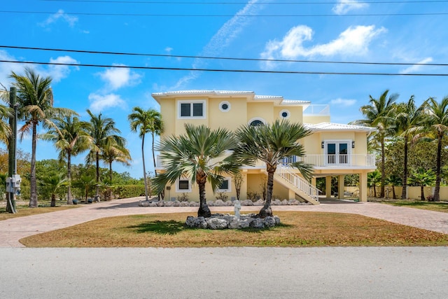 coastal home featuring stucco siding, stairway, decorative driveway, a carport, and french doors