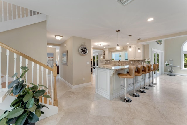 kitchen with baseboards, light stone counters, backsplash, visible vents, and a kitchen bar