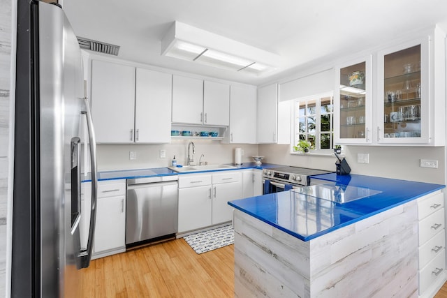 kitchen with a sink, a peninsula, appliances with stainless steel finishes, white cabinets, and light wood finished floors