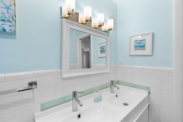 bathroom featuring tile walls, double vanity, a wainscoted wall, and a sink