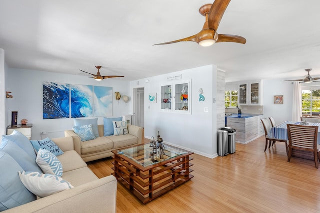 living area with baseboards, ceiling fan, and light wood finished floors