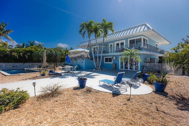 rear view of property with french doors, a pool, metal roof, a balcony, and a patio area