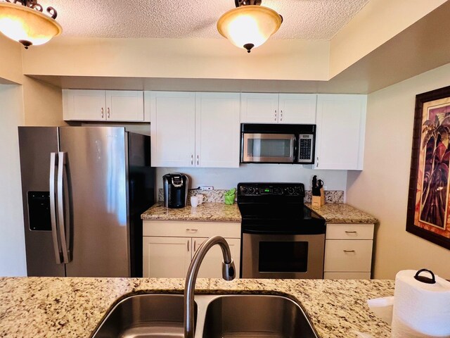 kitchen featuring a textured ceiling, appliances with stainless steel finishes, white cabinets, and a sink