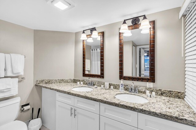 bathroom with toilet, double vanity, and a sink