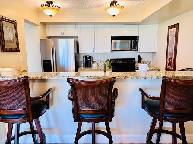 kitchen with light stone counters, stainless steel appliances, a peninsula, white cabinetry, and a kitchen bar