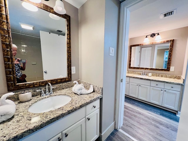 full bathroom featuring two vanities, a sink, visible vents, and wood finished floors