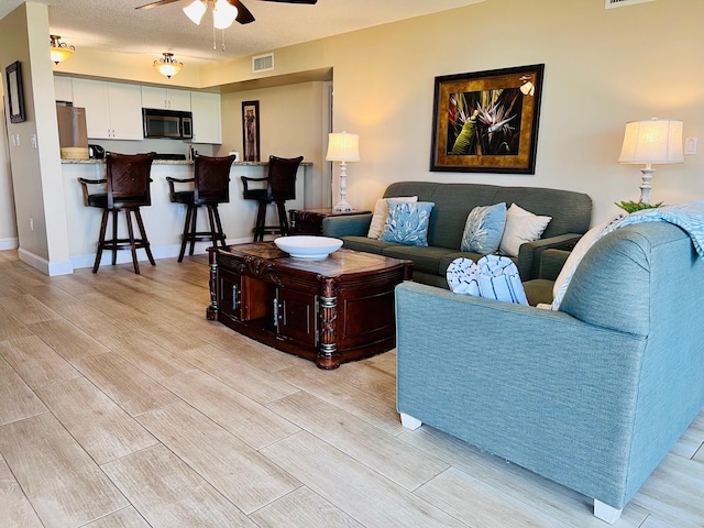 living area with baseboards, visible vents, a ceiling fan, and wood finish floors