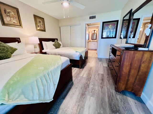 bedroom featuring baseboards, visible vents, wood finished floors, ensuite bathroom, and a closet