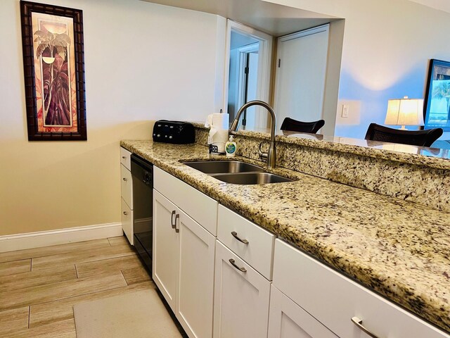 kitchen featuring light wood-style flooring, a sink, white cabinets, baseboards, and light stone countertops