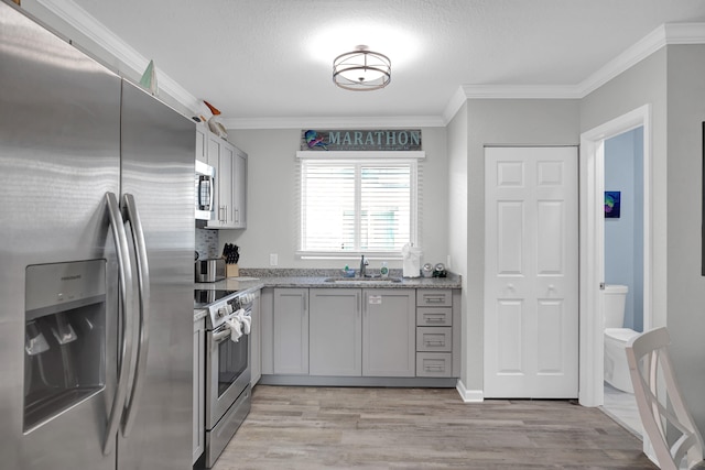 kitchen featuring light wood-style floors, crown molding, stainless steel appliances, and a sink