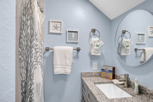 bathroom with a textured wall, curtained shower, and vanity