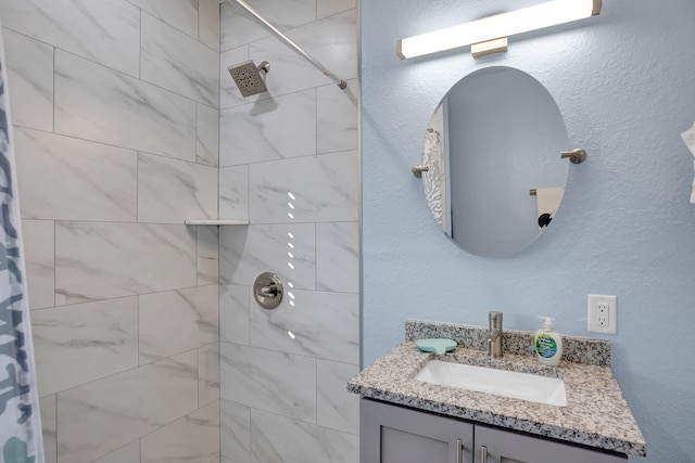 full bath featuring a textured wall, tiled shower, and vanity