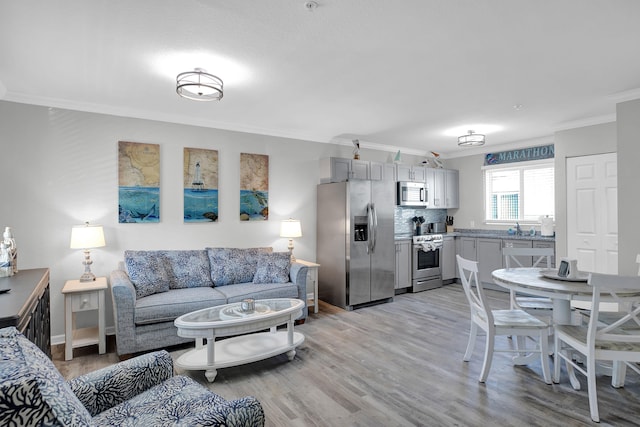 living area with ornamental molding, light wood-type flooring, and baseboards