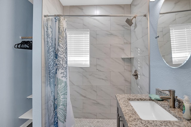 bathroom featuring a textured wall, tiled shower, and vanity