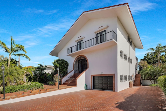 view of front of house featuring decorative driveway, stairway, a balcony, and stucco siding