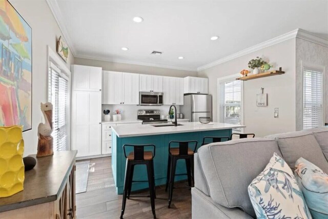 7202 Simran Ln, Duck, FL 33050 - kitchen with stainless steel appliances, a center island with sink, a kitchen bar, crown molding, and light wood-type flooring
