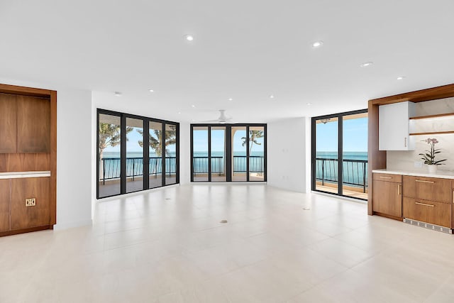 unfurnished living room featuring plenty of natural light, a water view, a wall of windows, and recessed lighting
